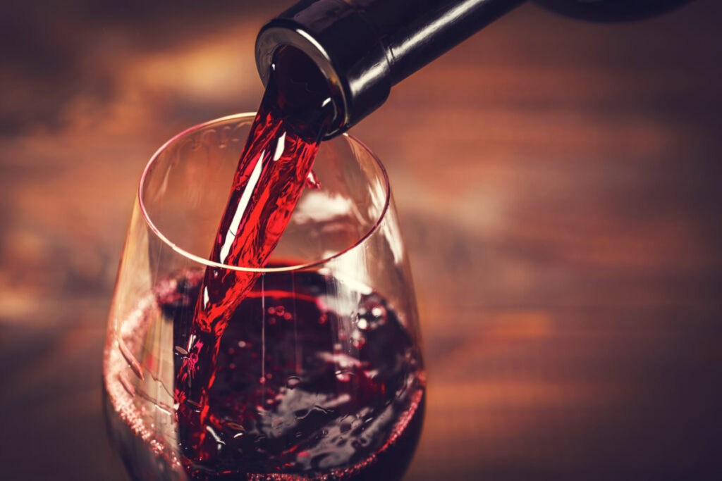 pouring,red,wine,into,the,glass,against,wooden,background